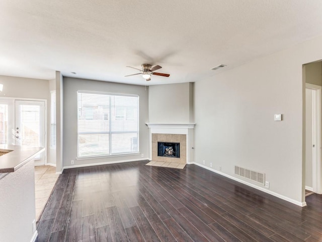 unfurnished living room with ceiling fan, visible vents, a tiled fireplace, and wood finished floors