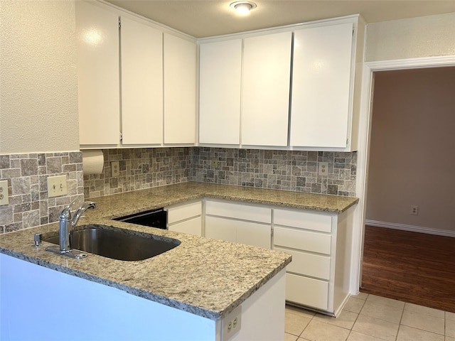 kitchen with white cabinets, light stone countertops, a sink, decorative backsplash, and light tile patterned floors