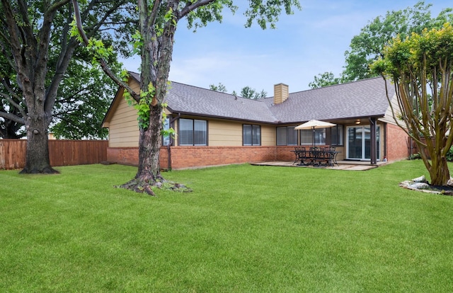 rear view of property with fence, a chimney, brick siding, and a lawn