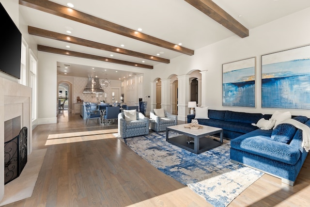 living area with arched walkways, beamed ceiling, a fireplace with flush hearth, and wood finished floors