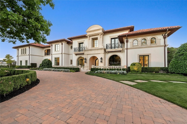 mediterranean / spanish home featuring curved driveway, stucco siding, a balcony, and a front yard