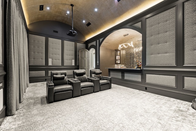 home theater room featuring a decorative wall, lofted ceiling, a chandelier, arched walkways, and carpet