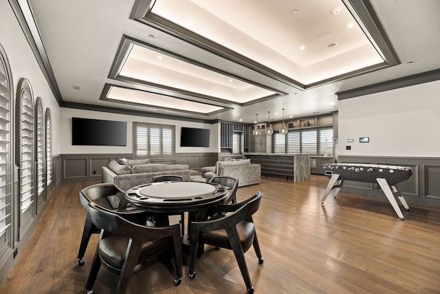 recreation room with crown molding, wainscoting, a decorative wall, wood finished floors, and a tray ceiling