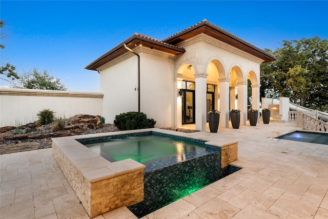 back of house with a tiled roof, an in ground hot tub, a patio area, and stucco siding