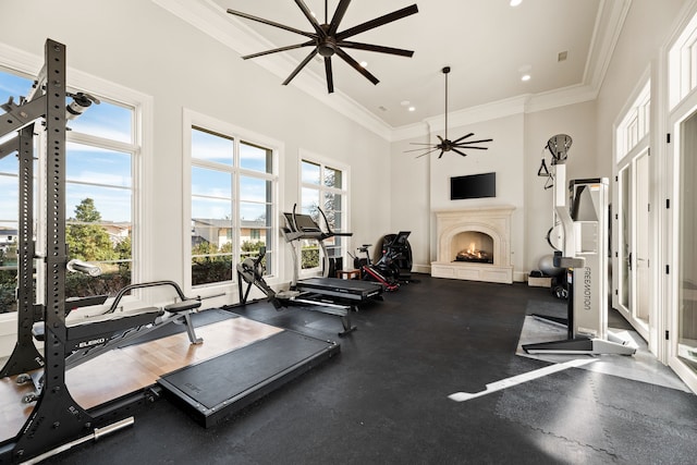 exercise room with ceiling fan, a lit fireplace, a wealth of natural light, and a towering ceiling