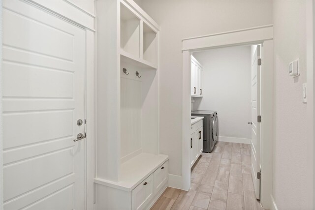 mudroom featuring baseboards, light wood-style flooring, and washing machine and clothes dryer