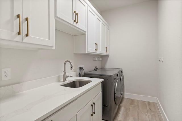 laundry area featuring cabinet space, independent washer and dryer, a sink, light wood-style flooring, and baseboards