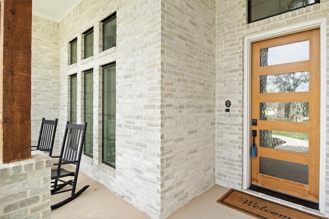 doorway to property with a porch and brick siding