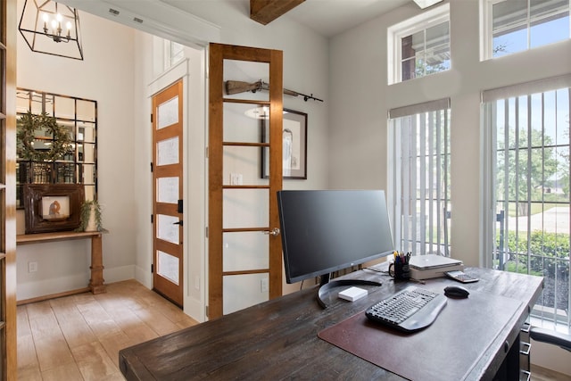 office space featuring light wood-style flooring, a notable chandelier, a high ceiling, and a wealth of natural light