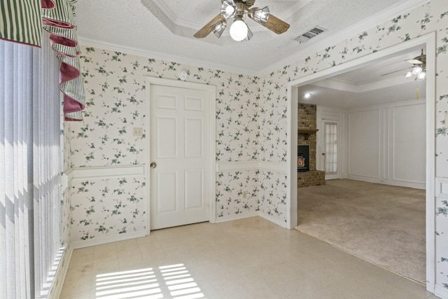 spare room with visible vents, crown molding, a brick fireplace, wallpapered walls, and a ceiling fan