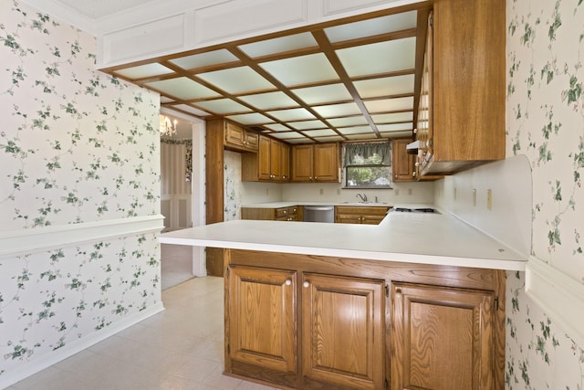 kitchen with brown cabinetry, stainless steel dishwasher, a sink, a peninsula, and wallpapered walls