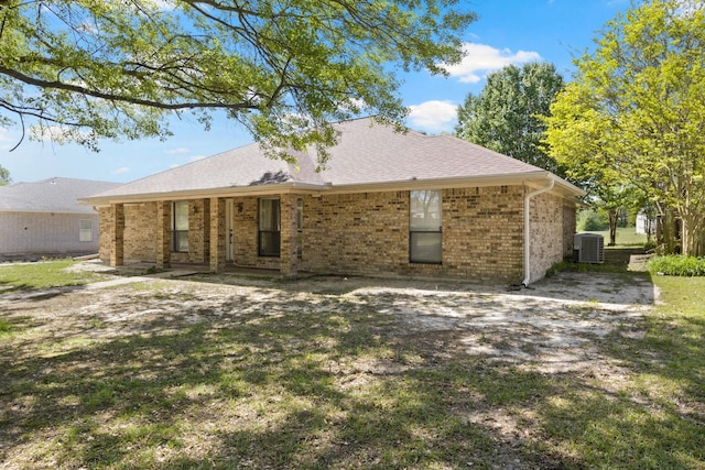 rear view of house with central air condition unit, a shingled roof, and brick siding