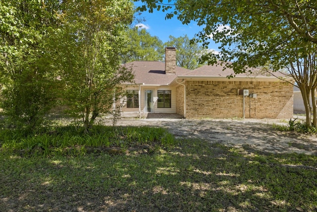 rear view of house with brick siding, a chimney, and roof with shingles