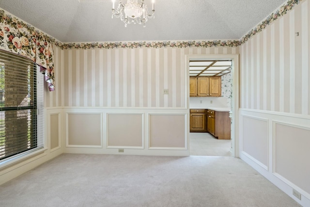 empty room featuring wainscoting, wallpapered walls, a textured ceiling, and a chandelier