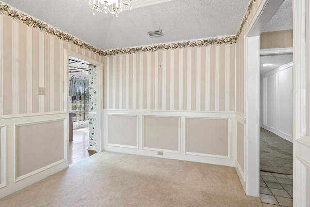 unfurnished room with a textured ceiling, visible vents, a notable chandelier, carpet flooring, and wallpapered walls