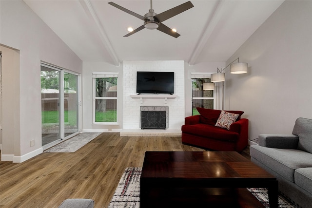 living room featuring a ceiling fan, a brick fireplace, wood finished floors, baseboards, and vaulted ceiling with beams