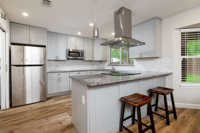 kitchen featuring plenty of natural light, island exhaust hood, visible vents, appliances with stainless steel finishes, and a peninsula