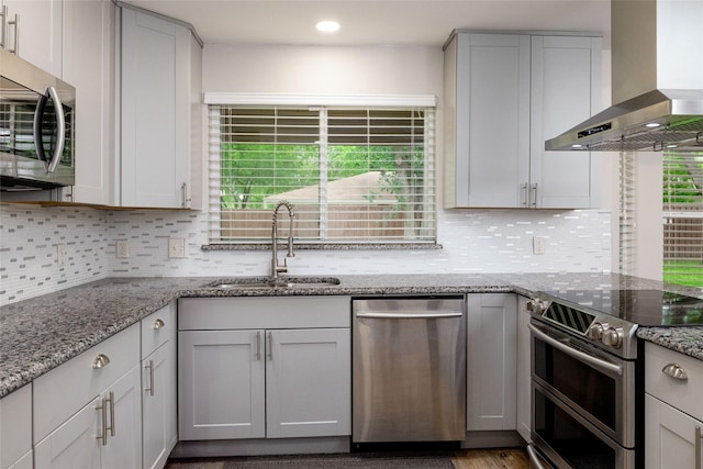 kitchen featuring wall chimney range hood, appliances with stainless steel finishes, plenty of natural light, and a sink