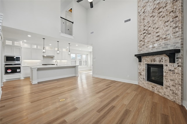 1851 Rosedale Ave, Van Alstyne, TX 75495 - unfurnished living room featuring light wood finished floors, ceiling fan, visible vents, a towering ceiling, and a fireplace