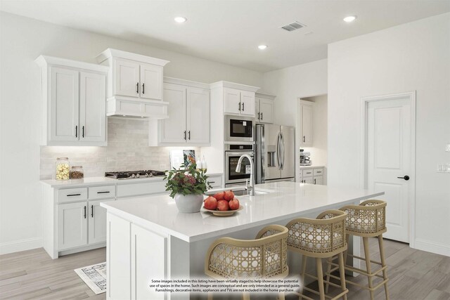 801 Daisy Corner Dr, Little Elm, TX 76227 - kitchen with stainless steel appliances, light wood-style flooring, tasteful backsplash, a center island with sink, and recessed lighting