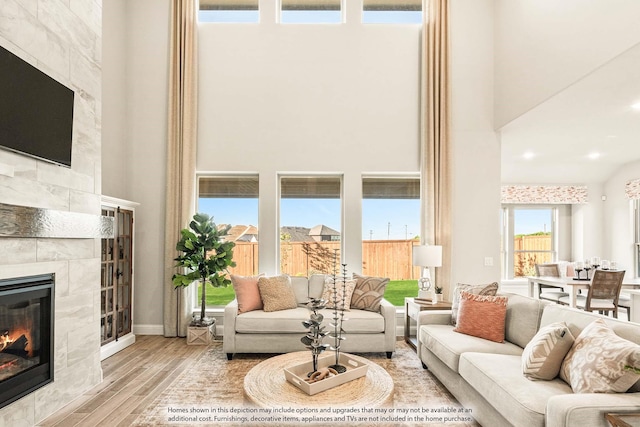 living room with baseboards, a high ceiling, a tiled fireplace, and wood finished floors