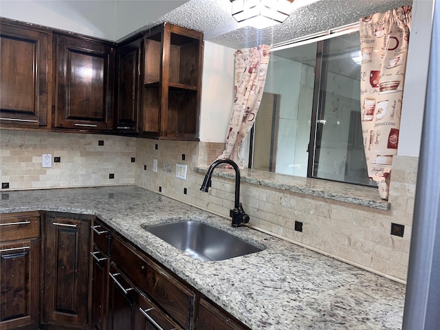 1005 Bass Dr, Plano, TX 75025 - kitchen featuring dark brown cabinetry, backsplash, open shelves, light stone countertops, and a sink