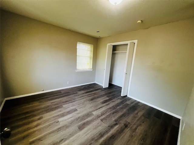 unfurnished bedroom featuring baseboards, dark wood-style floors, and a closet