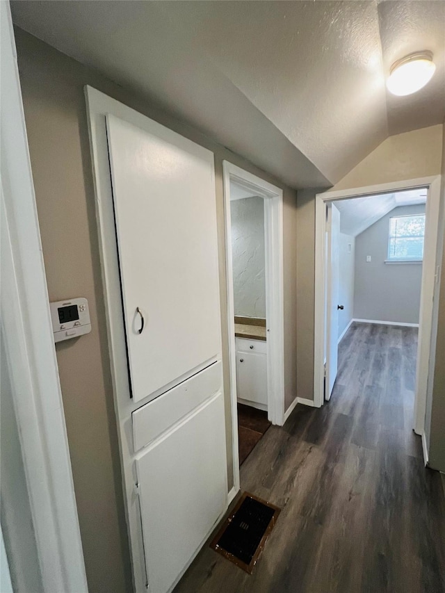 hallway featuring baseboards, a textured ceiling, lofted ceiling, and dark wood-style floors