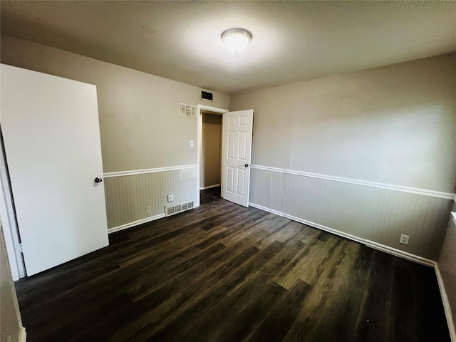 empty room with visible vents, dark wood-style flooring, and a wainscoted wall