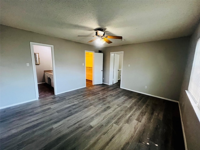 unfurnished bedroom featuring a textured ceiling, baseboards, a spacious closet, and dark wood-type flooring