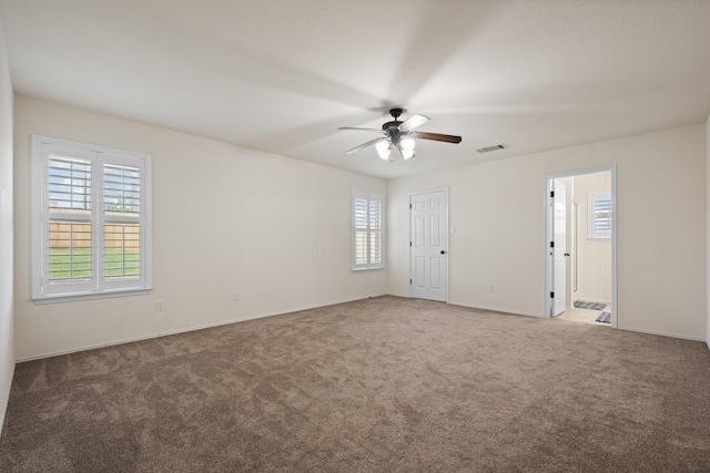 carpeted spare room with visible vents, a ceiling fan, and baseboards