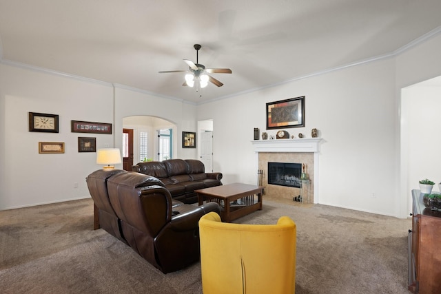living area with carpet flooring, crown molding, ceiling fan, arched walkways, and a tiled fireplace
