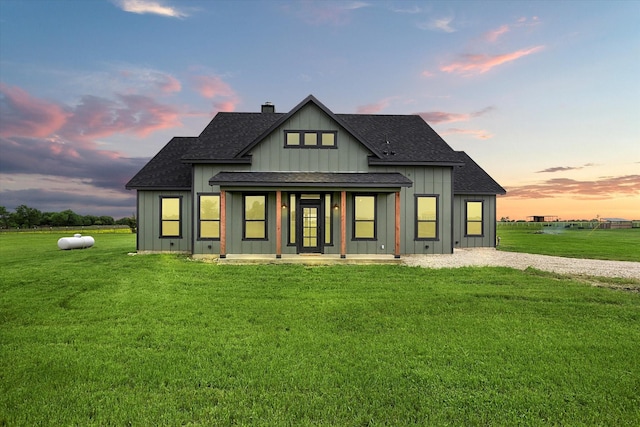 back of house at dusk with a lawn, board and batten siding, and roof with shingles