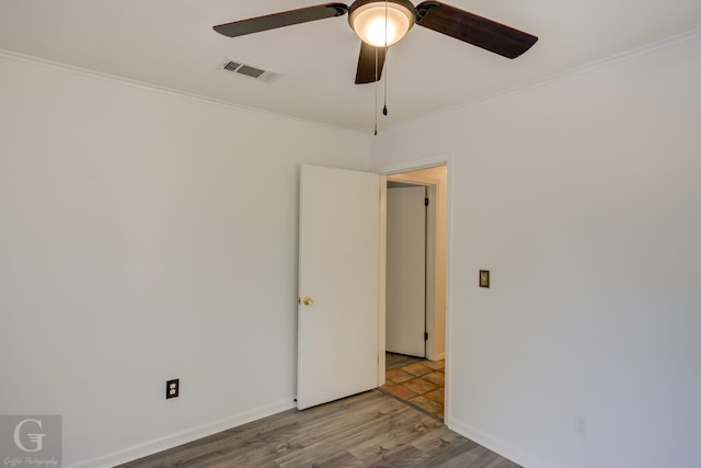 empty room featuring crown molding, ceiling fan, baseboards, wood finished floors, and visible vents