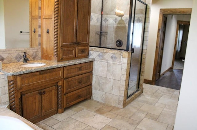 full bath with vanity, a shower stall, stone tile flooring, and tile walls