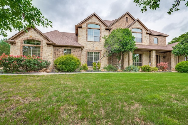 view of front of property featuring brick siding, a shingled roof, a front lawn, and stone siding