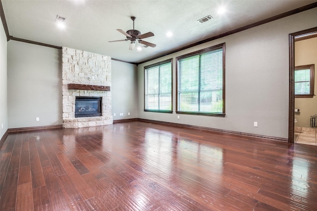 unfurnished living room featuring visible vents, ornamental molding, wood finished floors, a stone fireplace, and a ceiling fan