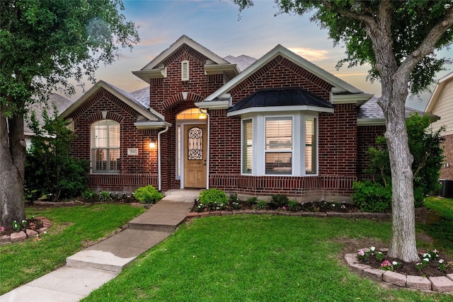 view of front of home with brick siding, central AC, and a yard