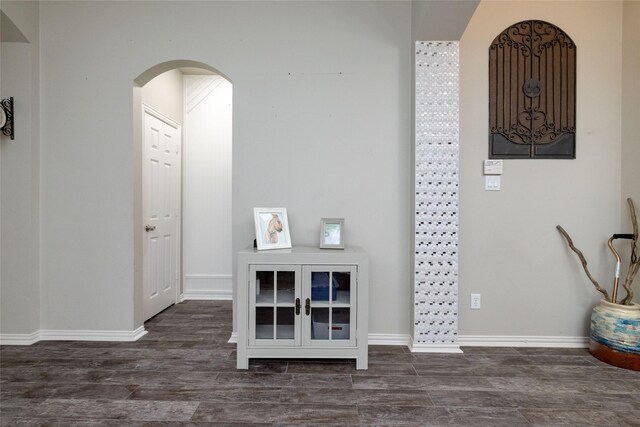 foyer entrance with arched walkways, baseboards, and wood finished floors