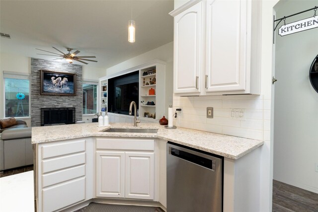 kitchen featuring stainless steel dishwasher, a ceiling fan, a peninsula, a tile fireplace, and a sink