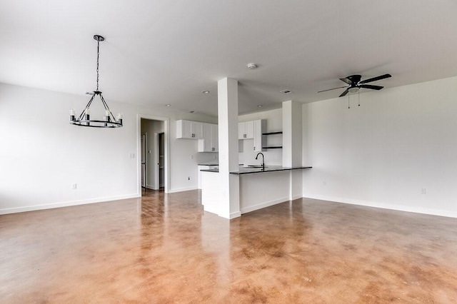 unfurnished living room with ceiling fan with notable chandelier, baseboards, concrete flooring, and a sink