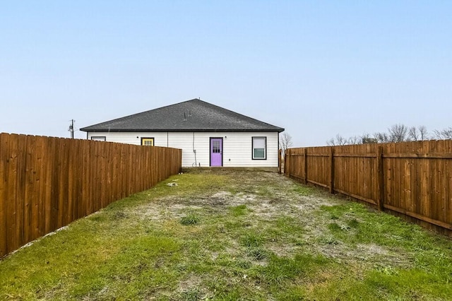 rear view of property featuring a shingled roof and a fenced backyard