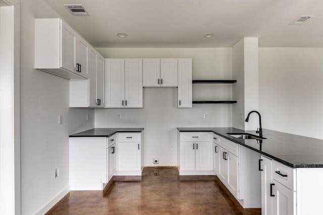 kitchen with a sink, concrete floors, a peninsula, and visible vents