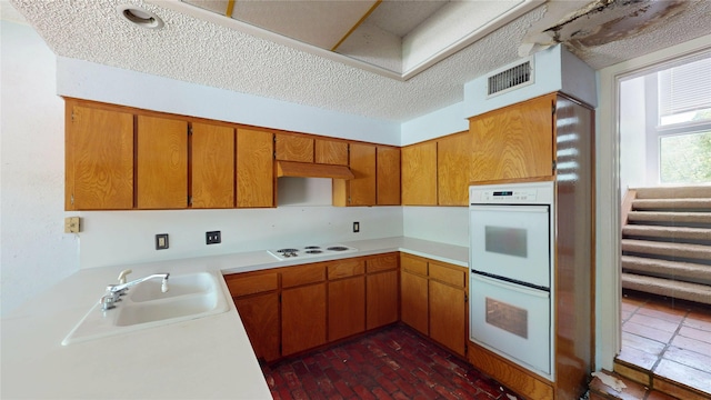 kitchen featuring visible vents, white appliances, light countertops, brown cabinets, and a sink