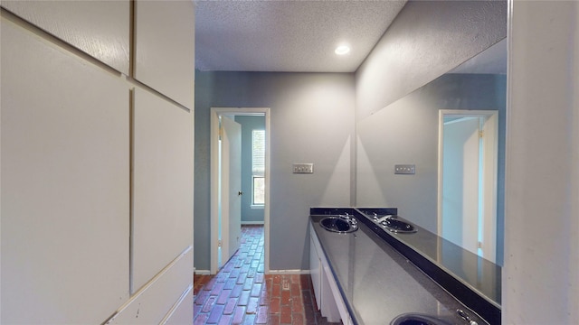 corridor featuring a sink, baseboards, brick floor, and a textured ceiling