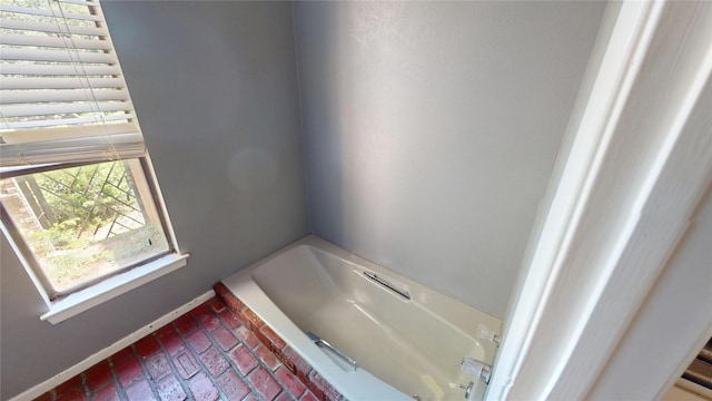 bathroom with baseboards, brick floor, and a bathing tub