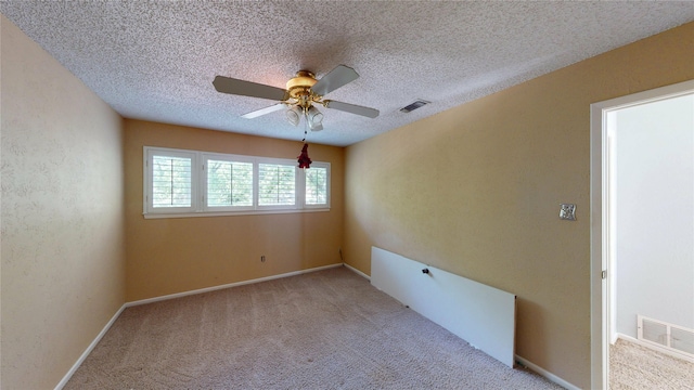 carpeted spare room featuring a ceiling fan, a textured ceiling, visible vents, and baseboards