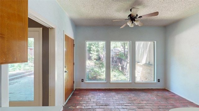 empty room with a ceiling fan, a textured ceiling, baseboards, and brick floor