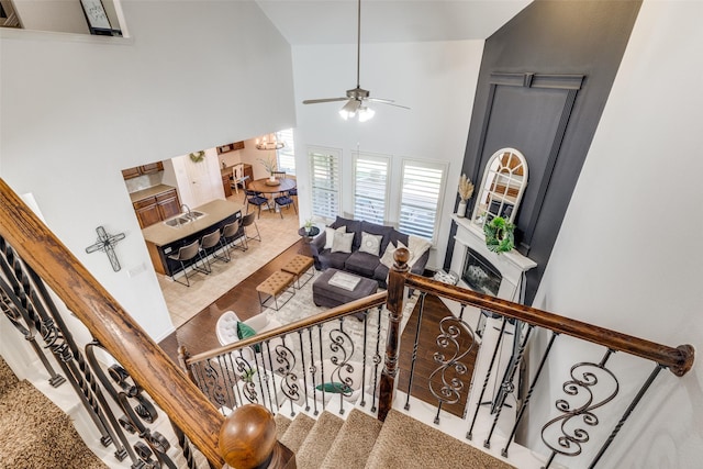 staircase featuring high vaulted ceiling, a glass covered fireplace, and ceiling fan