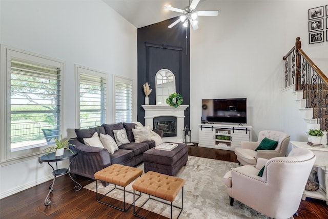 living room featuring dark wood-style flooring, ceiling fan, high vaulted ceiling, a glass covered fireplace, and stairway